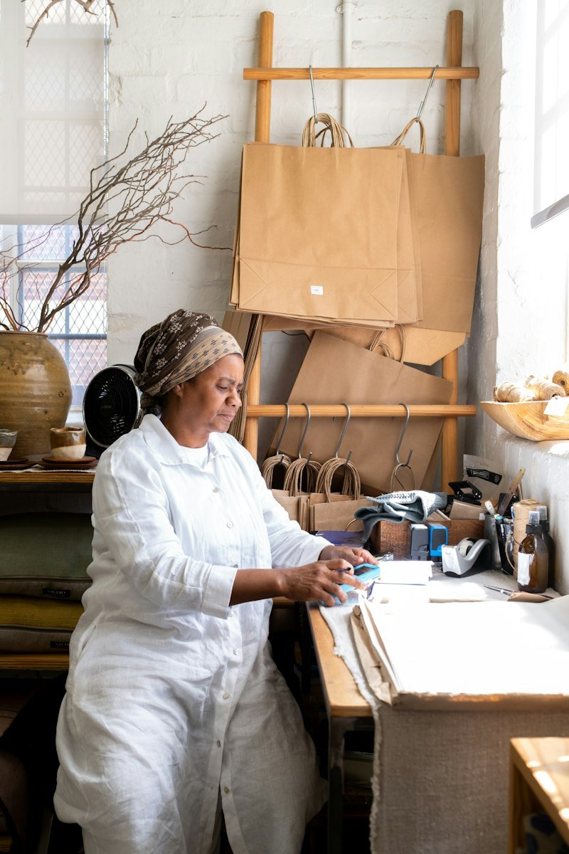 A maker in white workwear working at her bench in a bright studio