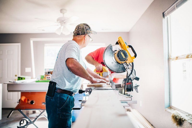 A carpenter cutting timber at a miter saw in a house under renovation